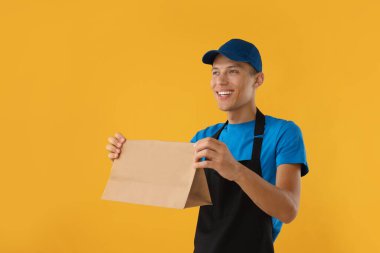 Turuncu arka planda kağıt torbası olan fast food işçisi.