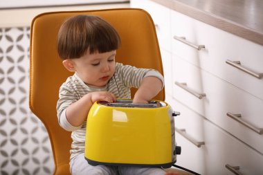 Küçük çocuk mutfakta tost makinesiyle oynuyor. Tehlikeli bir durum.