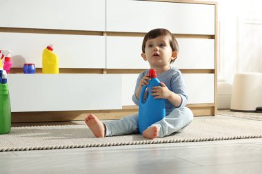 Evdeki dolabın yanında deterjan şişeleriyle oynayan küçük bir çocuk. Çocuk tehlikede.