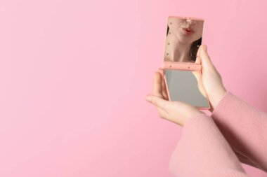 Pembe arka planda cep aynası tutan kadın, yakın plan. Metin için boşluk