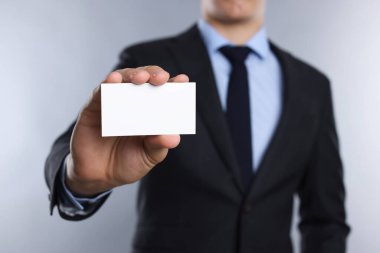 Gri arka planda boş bir kartvizit tutan adam, yakın plan. Tasarım için model