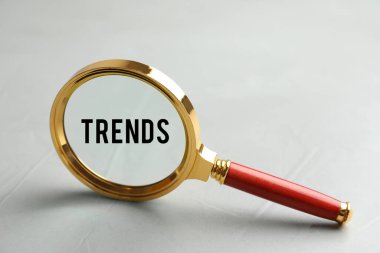 Gri arka planda büyüteçteki kelime eğilimleri, yakın plan. Yeni ve popüler fikirler arama kavramı