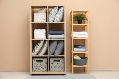 Ev yapımı tekstil organizasyonu. Bej duvarın yanındaki raflarda farklı yastıklar, çarşaflar ve battaniyeler var.