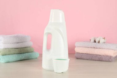 Çamaşır deterjanı, kep, temiz havlular ve ahşap masada pembe arka planda duran pamuk çiçeklerle dolu bir şişe.