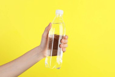 Sarı arka planda plastik su şişesi tutan kadın, yakın plan. Metin için boşluk