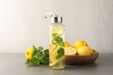 Şişe içinde naneli limon suyu, açık gri masada taze meyve ve yapraklar.