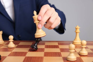 Satranç tahtasında açık gri arka planda satranç oynayan iş adamı, yakın plan. Rekabet konsepti