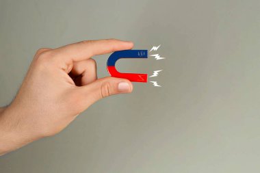 Gri arka planda yıldırımlar olan at nalı mıknatısı tutan adam, yakın plan. Metin için boşluk