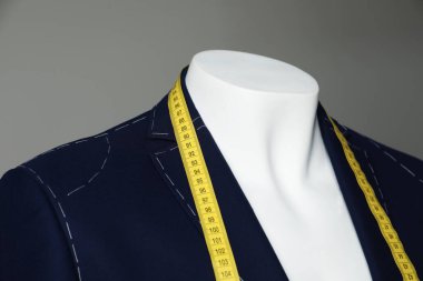 Semi-ready jacket with tailor's measuring tape on mannequin against grey background, closeup clipart