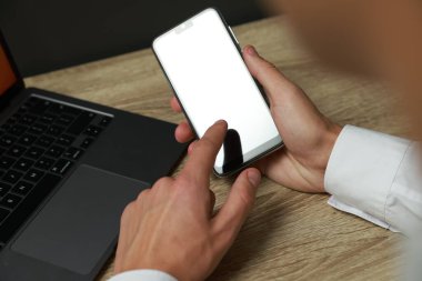 Adam ahşap masada boş ekranlı akıllı telefon kullanıyor.