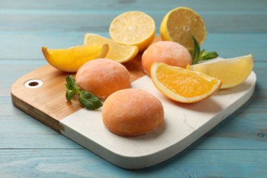 Board with tasty mochi, cut orange, lemon and mint on light blue wooden table, closeup clipart