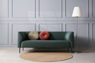 Gri duvarın yanında rahat bir kanepe ve lamba.