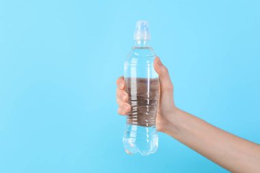 Açık mavi arka planda plastik su şişesi tutan kadın, yakın plan.
