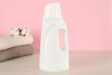 Çamaşır deterjanı, elbiseler ve pamuk çiçeklerle dolu bir şişe pembe arka planda.