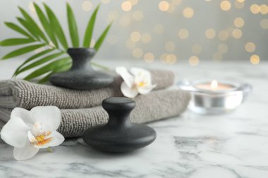 Spa taşları, orkide çiçekleri, havlular, yanan mum ve yaprak beyaz mermer masa, yakın çekim