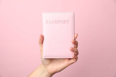 Pasaportu elinde tutan kadın pembe arka planda, yakın plan.