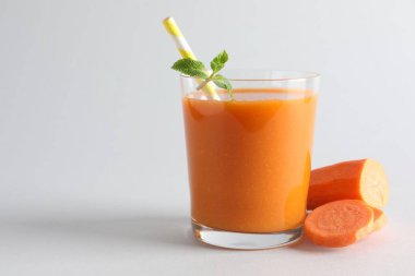 Cam içinde taze havuç püresi ve açık gri arka planda kesilmiş sebze, yakın plan. Metin için boşluk