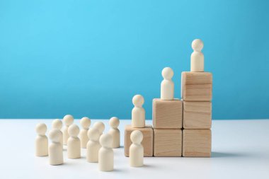 Beyaz masadaki ahşap bloklardaki insan figürleri açık mavi arka plana karşı. Rekabet konsepti
