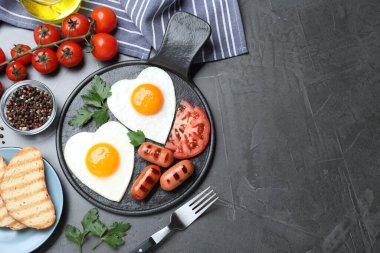 Koyu gri masada servis edilen kalp şeklinde sahanda yumurta ve sosislerle nefis bir kahvaltı. Metin için boşluk