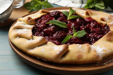 Kirazlı lezzetli galet ve açık mavi ahşap masa üzerinde nane, yakın plan.