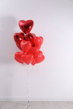 Beyaz duvarın yanında bir grup kalp şeklinde balon. Sevgililer Günü kutlaması