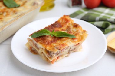 Lezzetli pişmiş lazanya. Fesleğenli beyaz masa, yakın plan.