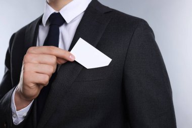 Gri arka planda ceketinin cebinden boş kartvizit alan adam, yakın plan. Tasarım için model