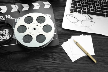 Movie clapper, film reel and laptop on black wooden table, above view clipart