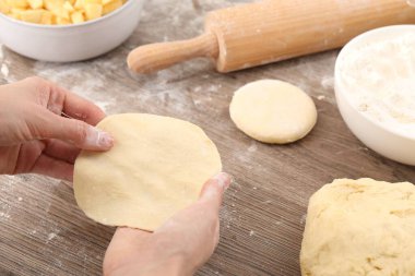 Making pirozhki (stuffed pastry pies). Woman with dough at wooden table, closeup clipart