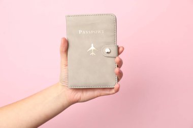 Pasaportu elinde tutan kadın pembe arka planda, yakın plan.