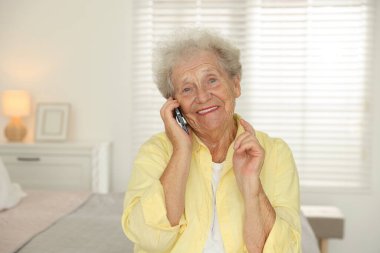 Gülümseyen son sınıf öğrencisi evde akıllı telefondan konuşuyor.