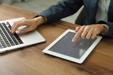 İş kadını, içerideki ahşap masada dizüstü bilgisayar ve tablet kullanıyor, yakın plan. Modern teknoloji