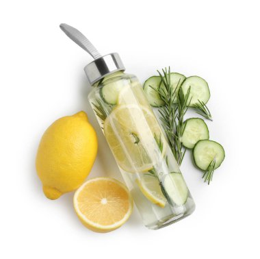 Şişe içinde limon suyu, biberiye, taze meyve ve beyaz arka planda salatalık dilimleri, üst manzara.