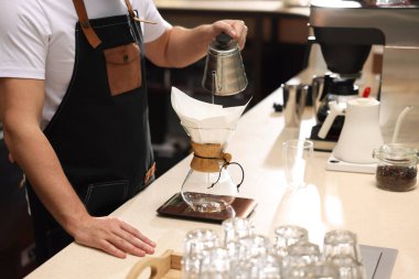 Barista kahve makinesinde kahve yapıyor. Kafedeki masada kağıt filtresi var. Yakın plan.