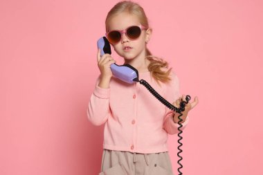 Pembe arka planda cep telefonu olan sevimli küçük bir kız.