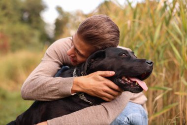 Gülümseyen adam dışarıda siyah sevimli köpeğe sarılıyor.