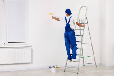 Erkek tamirci duvarları boyuyor, içeride paten kayıyor, arkadan bakıyor. Metin için boşluk