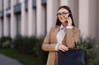 Şık takım elbiseli güzel bir kadın dışarıda akıllı telefondan konuşuyor. Metin için boşluk