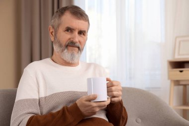 Evdeki kanepede bir fincan sıcak içecekle olgun bir adam.