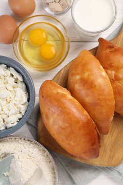 Lezzetli pirozhki (hamur tatlısı) ve beyaz ahşap masa üzerindeki malzemeler, düz yatıyordu.