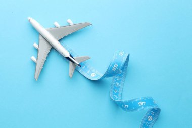 Plane model takes off and measuring tape as condensation trail on light blue background, top view clipart