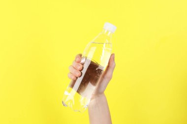 Sarı arka planda plastik su şişesi tutan kadın, yakın plan.