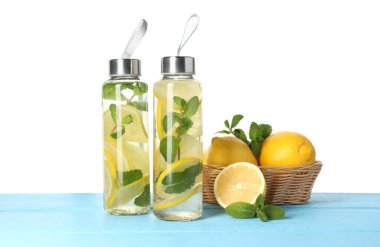 Şişe içinde naneli limon suyu, yapraklar ve açık mavi ahşap masada beyaz arka planda taze meyveler.