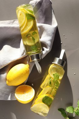 Şişe içinde naneli limon suyu, taze yapraklar ve açık kahverengi masada meyveler, düz uzanmış.