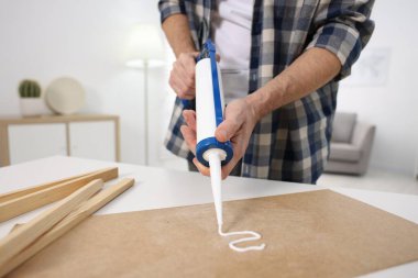 Man with caulking gun glueing plywood at white table indoors, closeup clipart