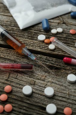 Drug addiction. Plastic bag with powder, syringes and pills on wooden table, closeup