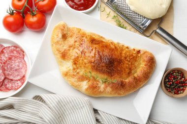 Lezzetli taze calzone pizza ve malzemeler beyaz masada, düz yerde.