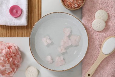 Bir kase çiçekli su ve beyaz mermer masa üzerinde farklı spa malzemeleri, düz yatıyordu.