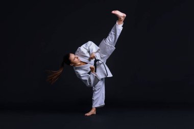 Kimonolu genç bir kadın siyah arka planda karate yapıyor.