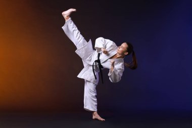 Kimonolu genç bir kadın karanlık arka planda karate yapıyor.